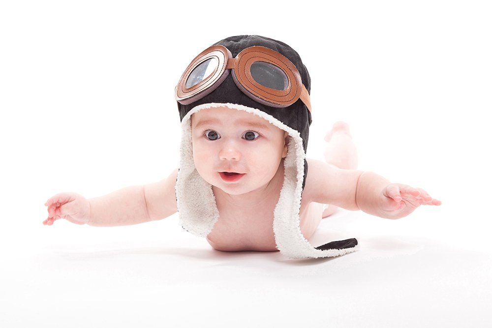 Naked cute smiling baby in the cap of the pilot is flying on a w
