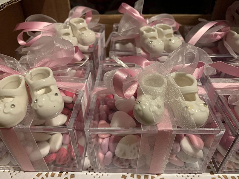 Scarpine da neonato in ceramica in scatole trasparenti con nastri rosa, piene di caramelle rosa e bianche come donazioni onlus, esposte per un baby shower. Scarpine da neonato in ceramica in scatole trasparenti con nastri rosa, piene di caramelle rosa e bianche come donazioni onlus, esposte per un baby shower.