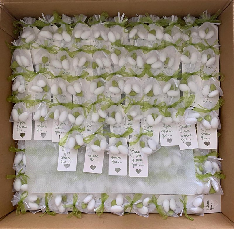 Scatola di cartone aperta piena di bomboniere confezionate singolarmente donate da una onlus, ciascuna legata con un nastro verde ed etichettata con i nomi degli invitati. Scatola di cartone aperta piena di bomboniere confezionate singolarmente donate da una onlus, ciascuna legata con un nastro verde ed etichettata con i nomi degli invitati.