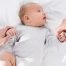 Un neonato che indossa una tutina a righe giace su una coperta bianca, tenendo per mano due adulti. Gli occhi del neonato sono spalancati, rivolti verso l'alto, forse in cerca di conforto da coliche gassose.