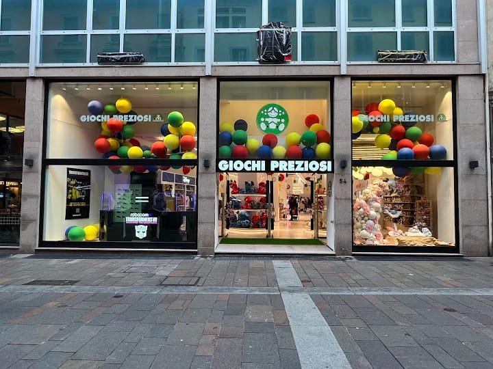 Veduta stradale del negozio di giocattoli Giochi Preziosi con decorazioni di palloncini colorati intorno alle vetrine e all'ingresso, che mostrano i giocattoli e la merce all'interno.