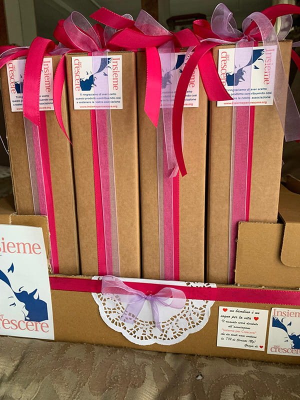 Un'esposizione di scatole regalo marroni decorate con nastri e centrini rosa, ognuna con l'etichetta "Insieme crescere" e un logo blu e rosa.