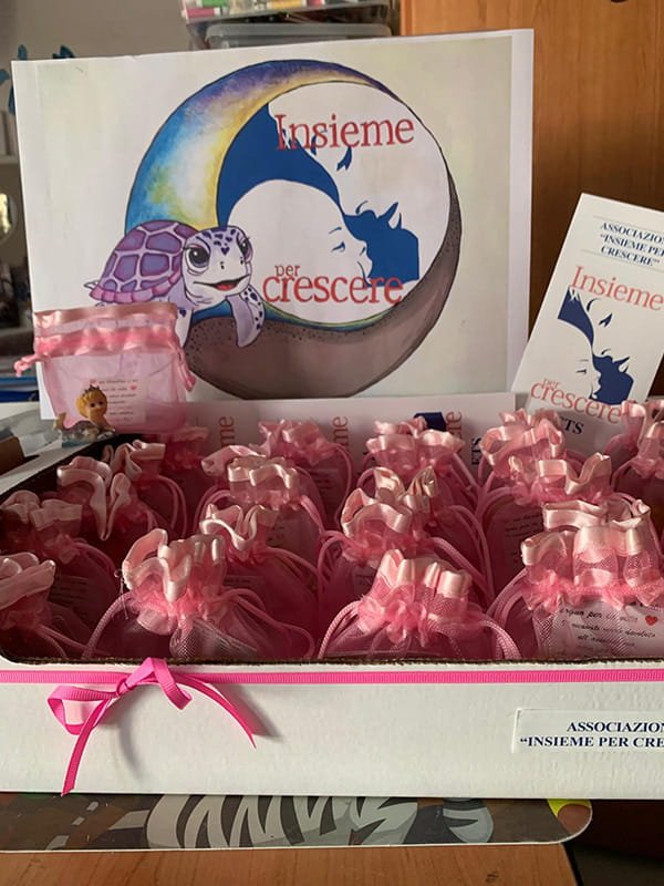 Un espositore pieno di buste regalo rosa è davanti a un cartello e a un volantino con il logo della tartaruga e il testo "Insieme per crescere".