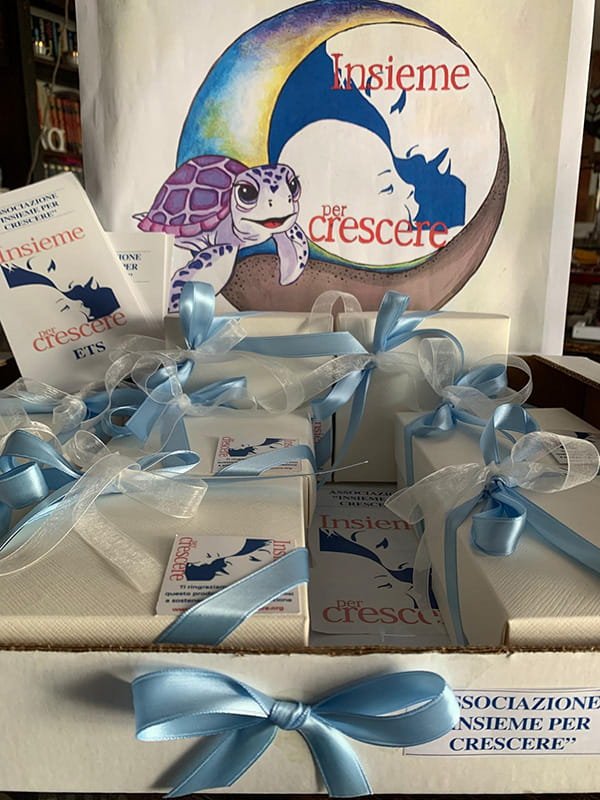 Un'esposizione di scatole regalo con nastri blu, un cartello e opuscoli con la scritta "Insieme per crescere" e opere d'arte con una tartaruga e una sagoma di genitore e figlio.